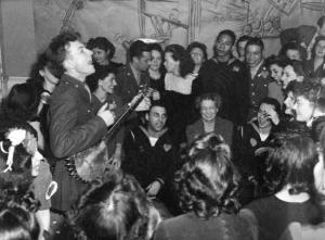 Peet Seeger singing in 1944 at the Washington Labor Canteen. Eleanor Roosevelt is seated in front between two service men.